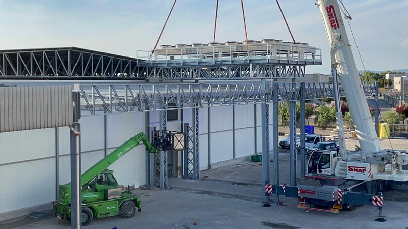 Crane lifting a unit with fans onto the steel structure of a plant